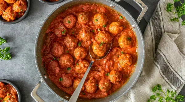 Sabrosas almondigas en salsa roja, recién servidas en una sartén, con perejil fresco espolvoreado. ¡Un plato casero irresistible!
