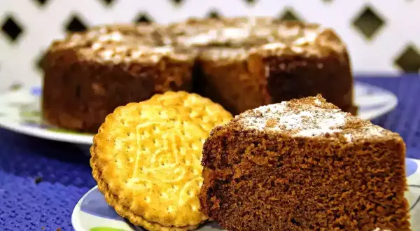 Un trozo de bizcocho de chocolate espolvoreado con azúcar glas junto a una galleta tipo Príncipe.