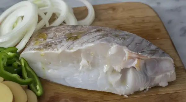 Filete de bacalao fresco con rodajas de patata, pimiento verde y cebolla, listo para preparar deliciosas recetas de bacalao.