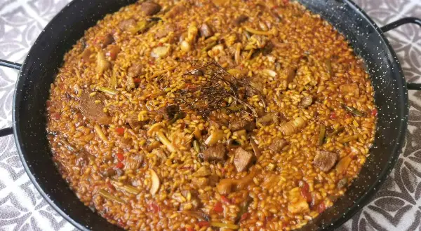 Arroz con secreto, un plato de paella con trozos de carne, pimientos y judías verdes, coronado con hierbas aromáticas.