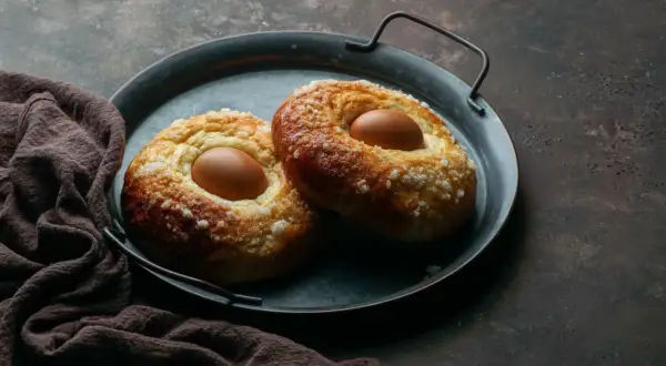Dos monas de Pascua esponjosas, cubiertas de azúcar, con un huevo cocido incrustado en cada una, listas para disfrutar.