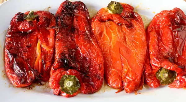 Pimientos rojos asados en freidora de aire, con piel arrugada y un brillo apetitoso.