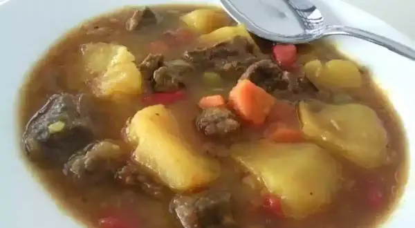 Un plato humeante de patatas con carne olla express, con trozos de zanahoria y pimiento rojo.