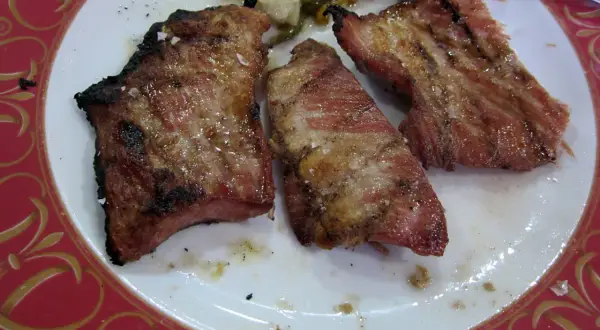 Tres jugosas porciones de secreto ibérico a la parrilla, con sal gruesa y un toque de pimienta, servidas en un plato blanco con borde rojo.