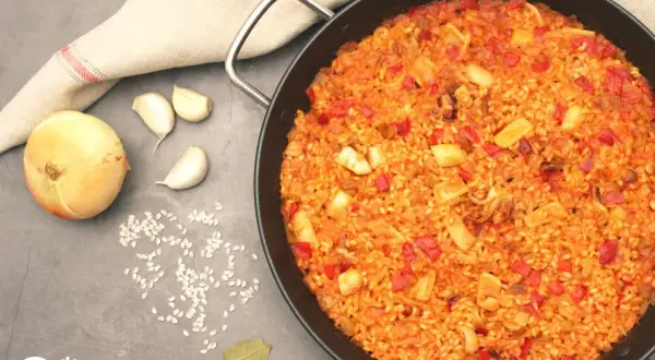 Paella de arroz con calamares, pimientos rojos y especias. Ingredientes frescos como cebolla y ajos acompañan este delicioso plato.