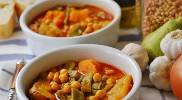 Dos cuencos de olla gitana murciana, un guiso tradicional con garbanzos, calabaza y judías verdes. Acompañado de pan y ingredientes frescos.