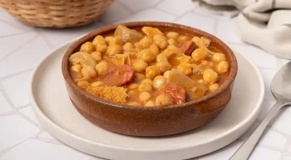 Un plato humeante de callos con garbanzos, chorizo y trozos de carne, servido en una cazuela de barro.