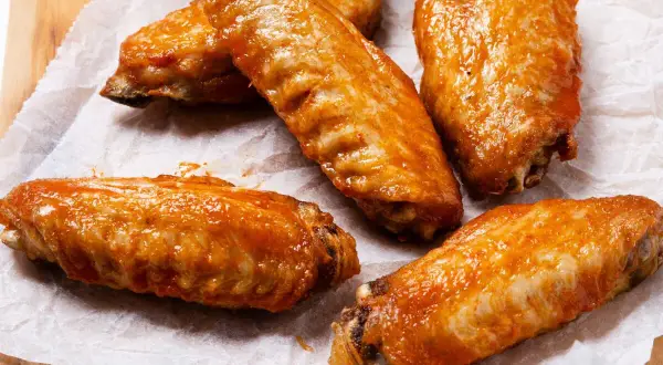 Cinco alitas de pollo al horno crujientes, cubiertas con una salsa brillante y apetitosa, listas para disfrutar.