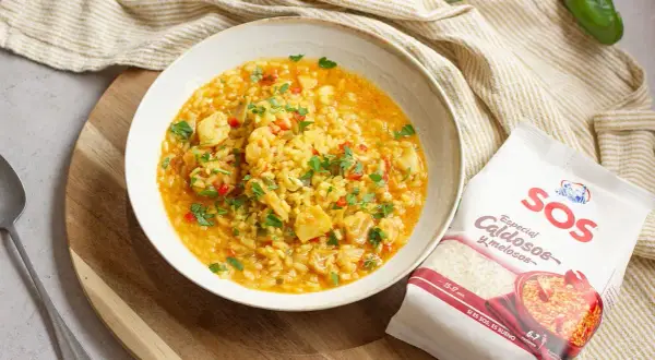 Un plato de arroz con bacalao, pimientos y perejil, acompañado de un paquete de arroz SOS especial caldosos.