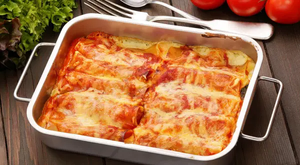 Canelones de atún gratinados en una bandeja metálica, listos para servir. Acompañados de tomates frescos y lechuga.