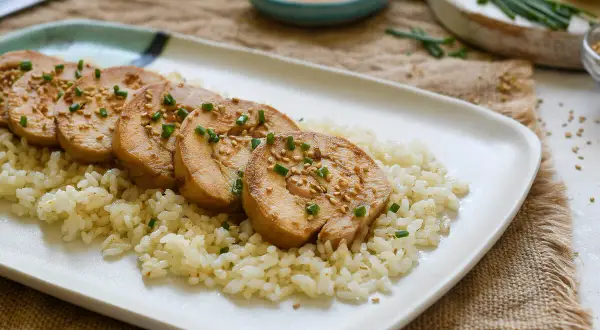 Pechuga de pollo en rodajas, servida sobre arroz blanco y espolvoreada con semillas de sésamo y cebollín.