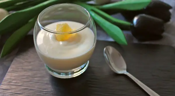 Delicioso postre de lemon curd en copa, decorado con un trozo de limón. Una cuchara plateada y tulipanes negros completan la escena.