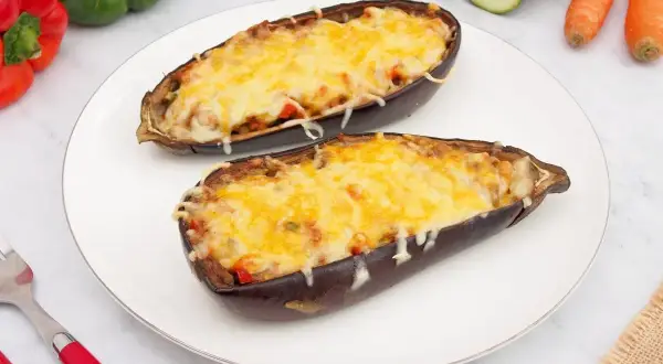 Dos mitades de berenjenas rellenas de verduras y cubiertas de queso gratinado, listas para disfrutar.