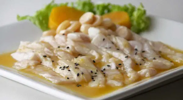Delicioso tiradito de corvina fresco, bañado en una salsa cítrica y adornado con semillas de sésamo negro, acompañado de camote y lechuga.