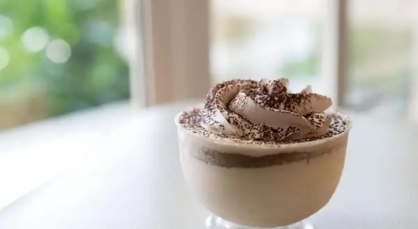 Delicioso mousse de café con crema batida y cacao espolvoreado, servido en un vaso transparente.
