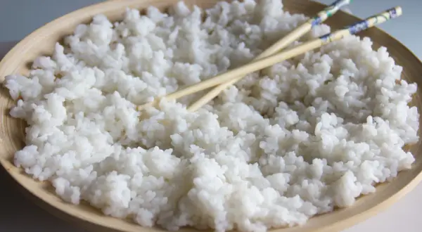 Arroz para sushi listo para preparar tus makis favoritos. Palillos cruzados sobre el arroz blanco y pegajoso en un cuenco de madera.
