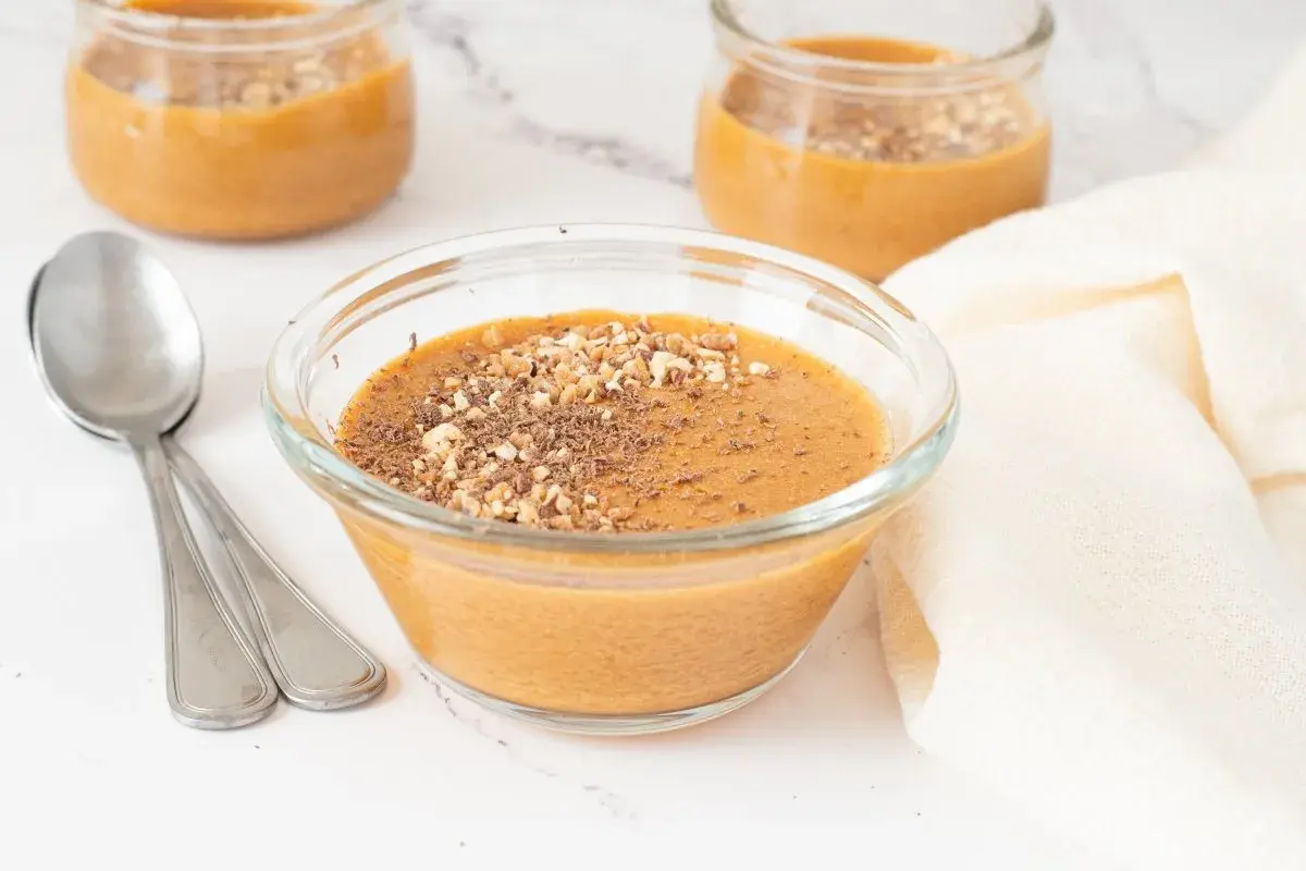 Delicioso postre cremoso, como baba de camelo, servido en un cuenco de cristal con nueces picadas y virutas de chocolate.