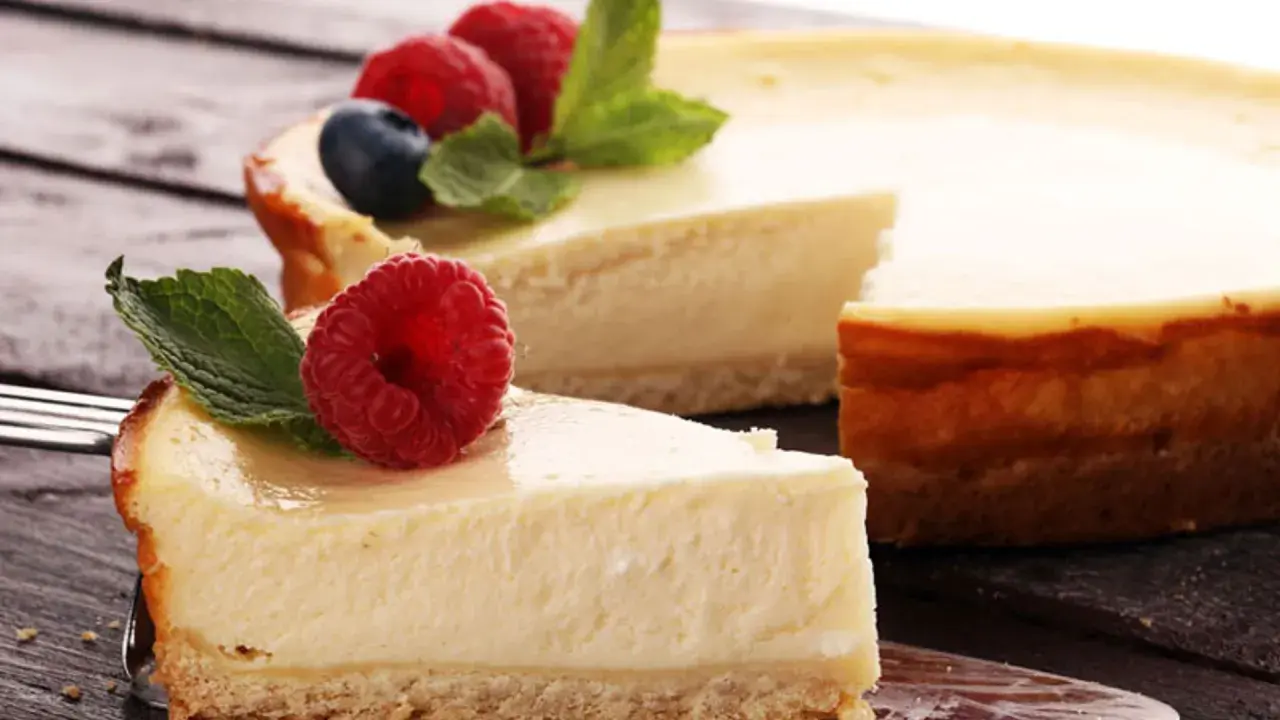 Deliciosa tarta de queso con galletas, coronada con frambuesas frescas y hojas de menta. Un trozo ya servido en un tenedor.
