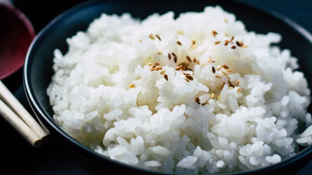 Un tazón de arroz blanco humeante, espolvoreado con semillas de sésamo, listo para ser disfrutado con palillos.