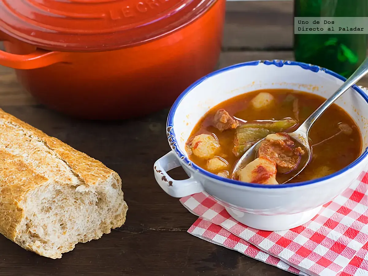 Un reconfortante plato de patatas a la riojana, con chorizo y pimientos, servido en un cuenco blanco con borde azul.