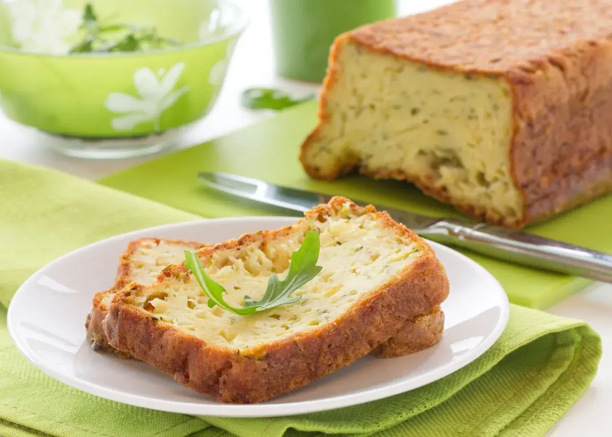 Rebanadas de un delicioso pastel de calabacín, esponjoso y dorado, servidas en un plato blanco con una hoja verde.