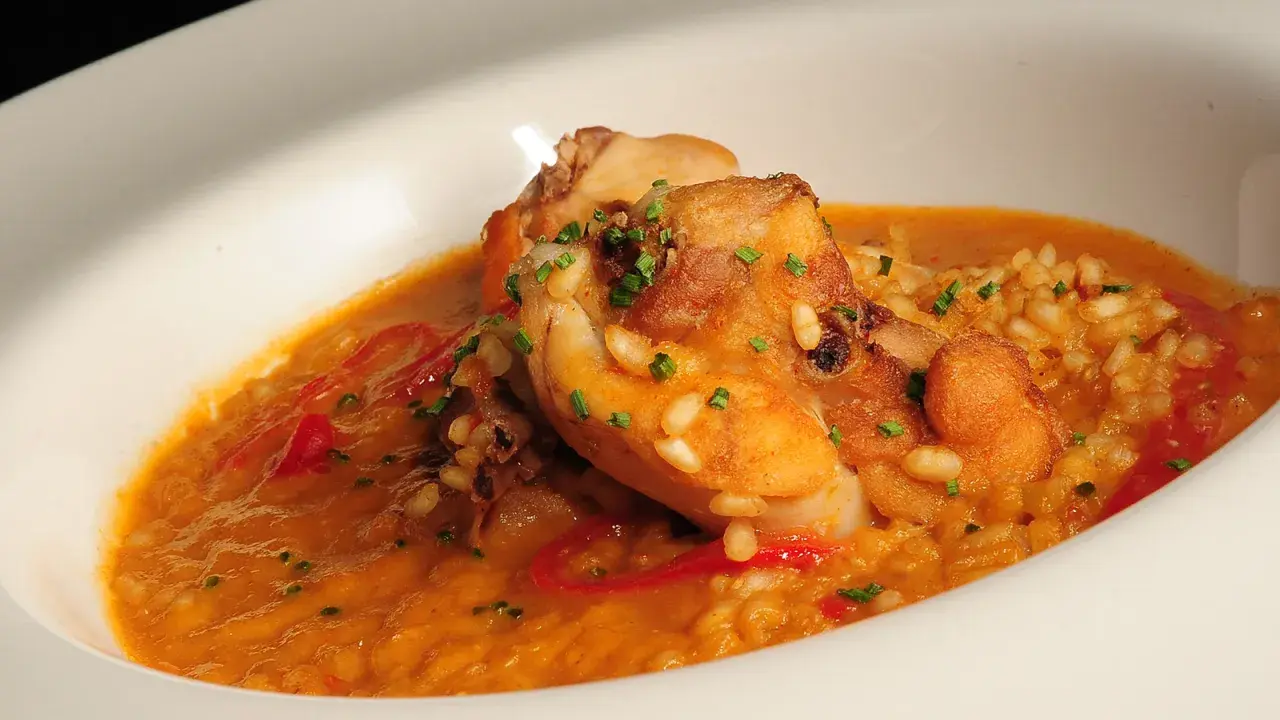 Delicioso arroz con conejo, trozos dorados de carne y pimientos rojos en una cremosa salsa, adornado con cebollino fresco.