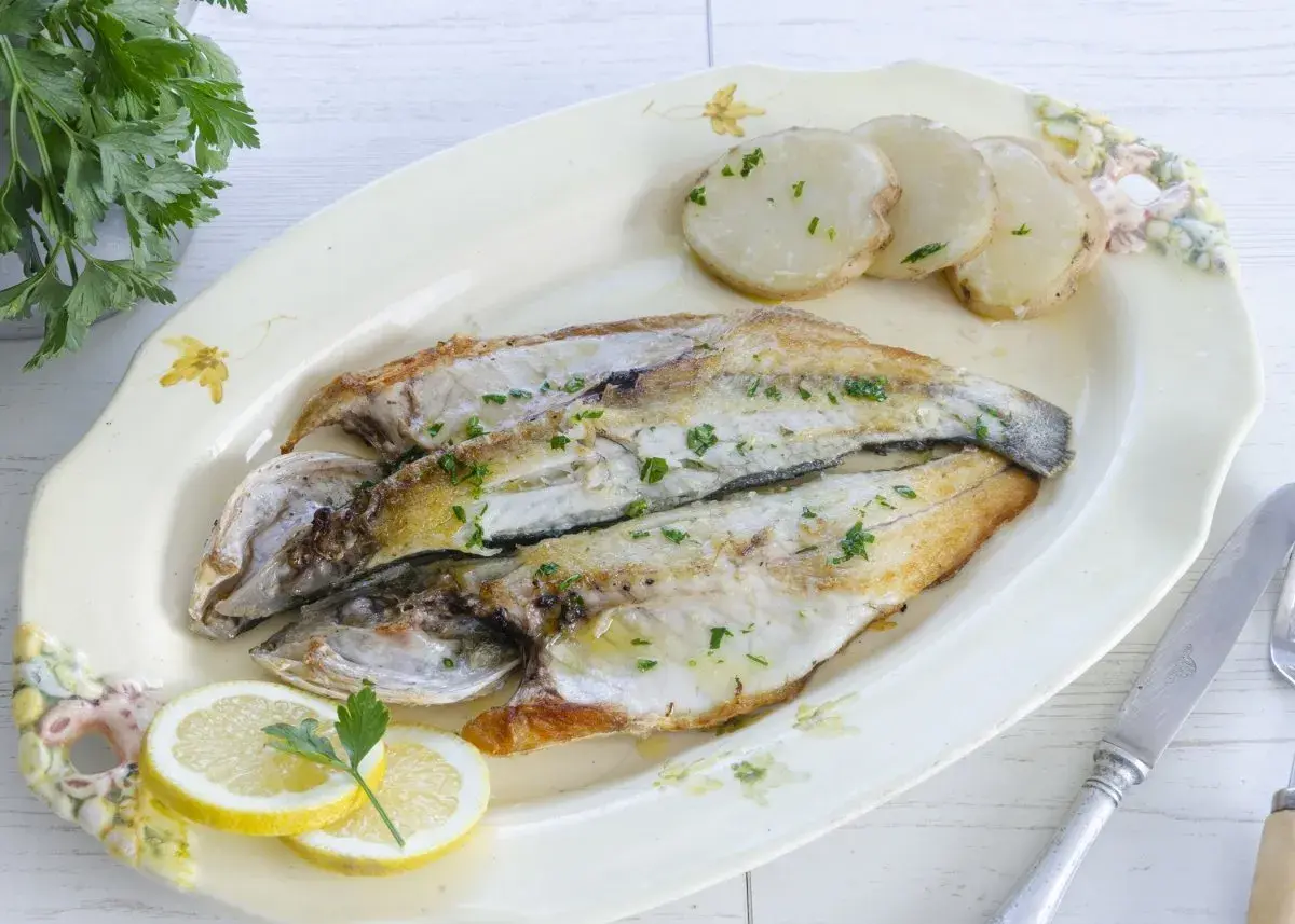 Lubina a la plancha, dorada y jugosa, servida con patatas y rodajas de limón. Un plato sencillo y delicioso.