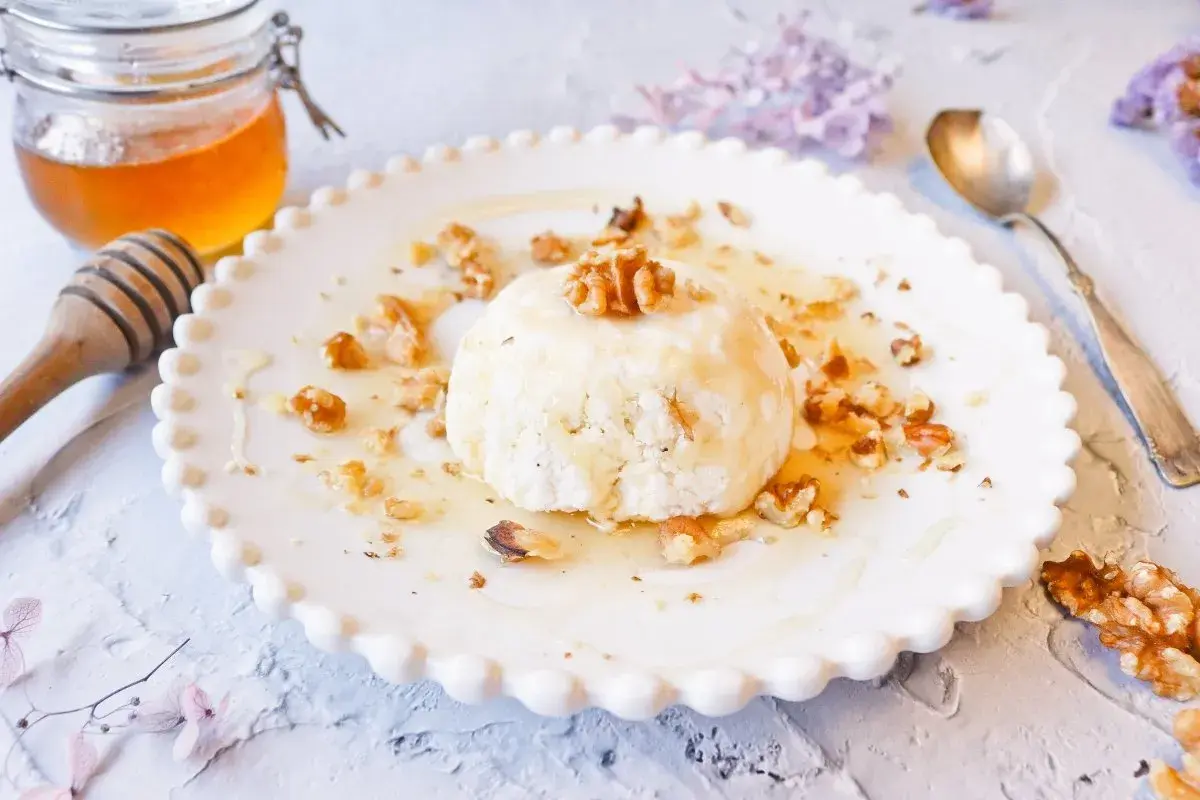 Delicioso postre de mel i mató con nueces y miel, servido en un plato blanco con borde festoneado.
