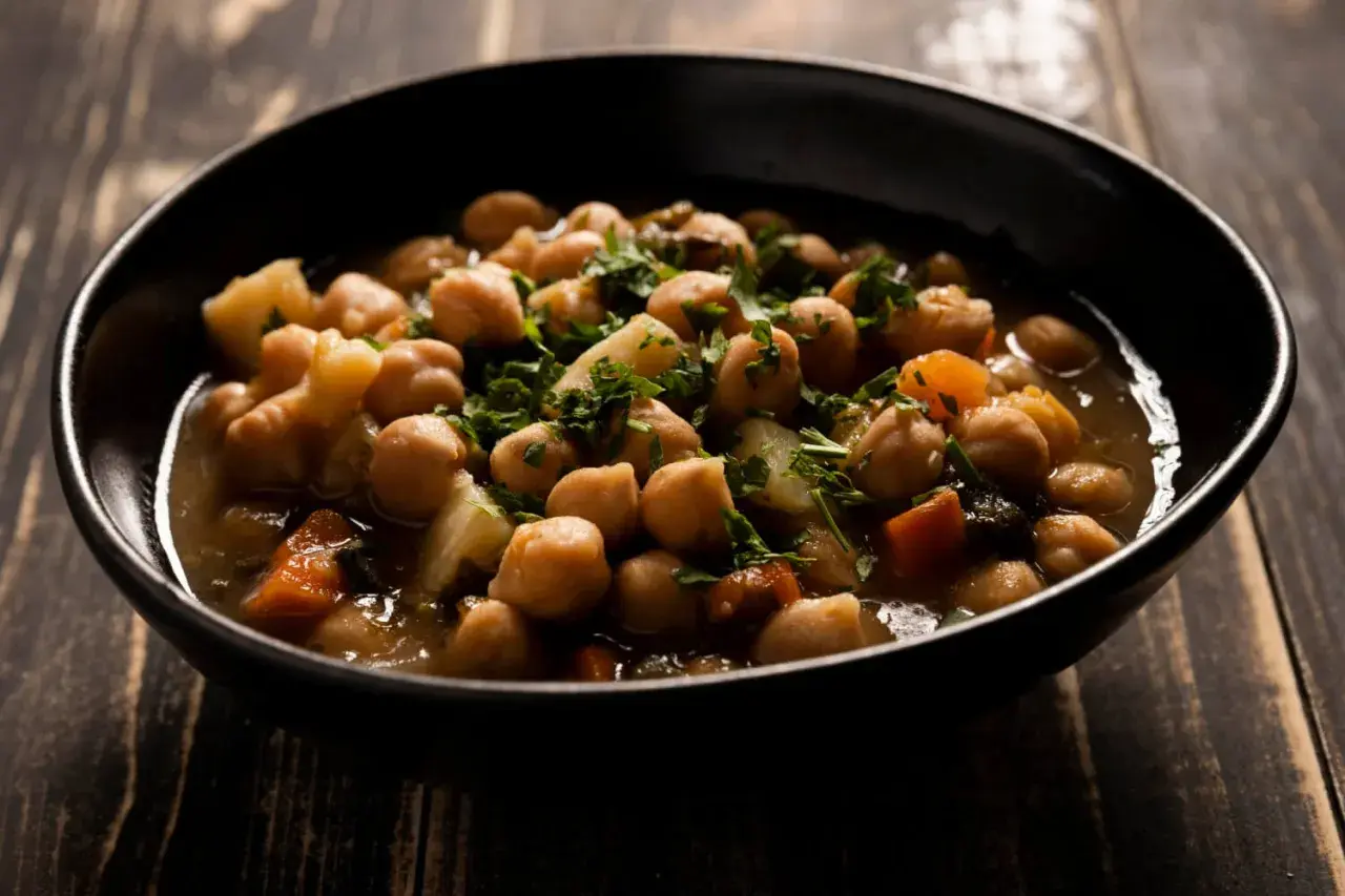Un tazón de garbanzos con patatas y zanahoria, adornado con perejil fresco. Una deliciosa receta de garbanzos tradicional.