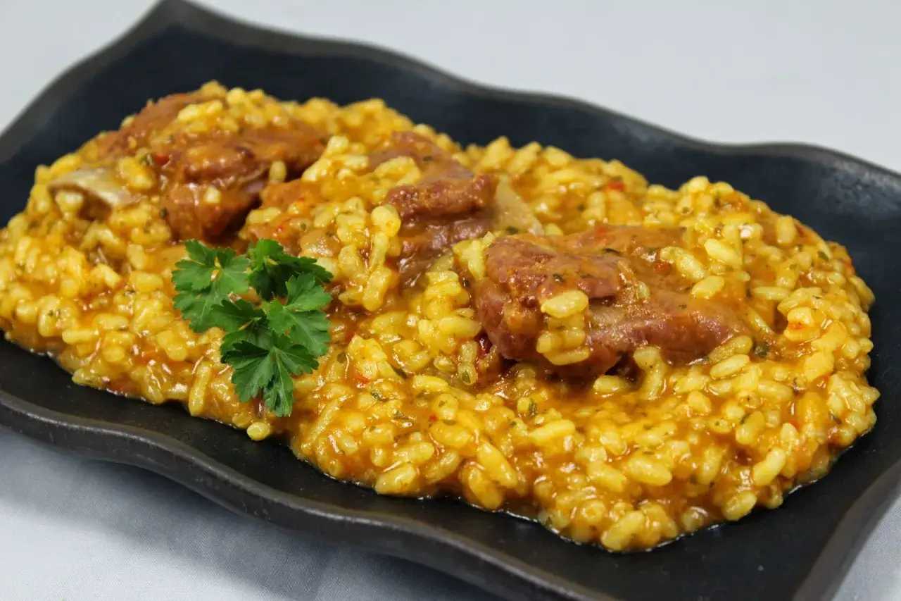Arroz con costillas jugosas, preparado en Thermomix, servido en plato negro con perejil fresco.