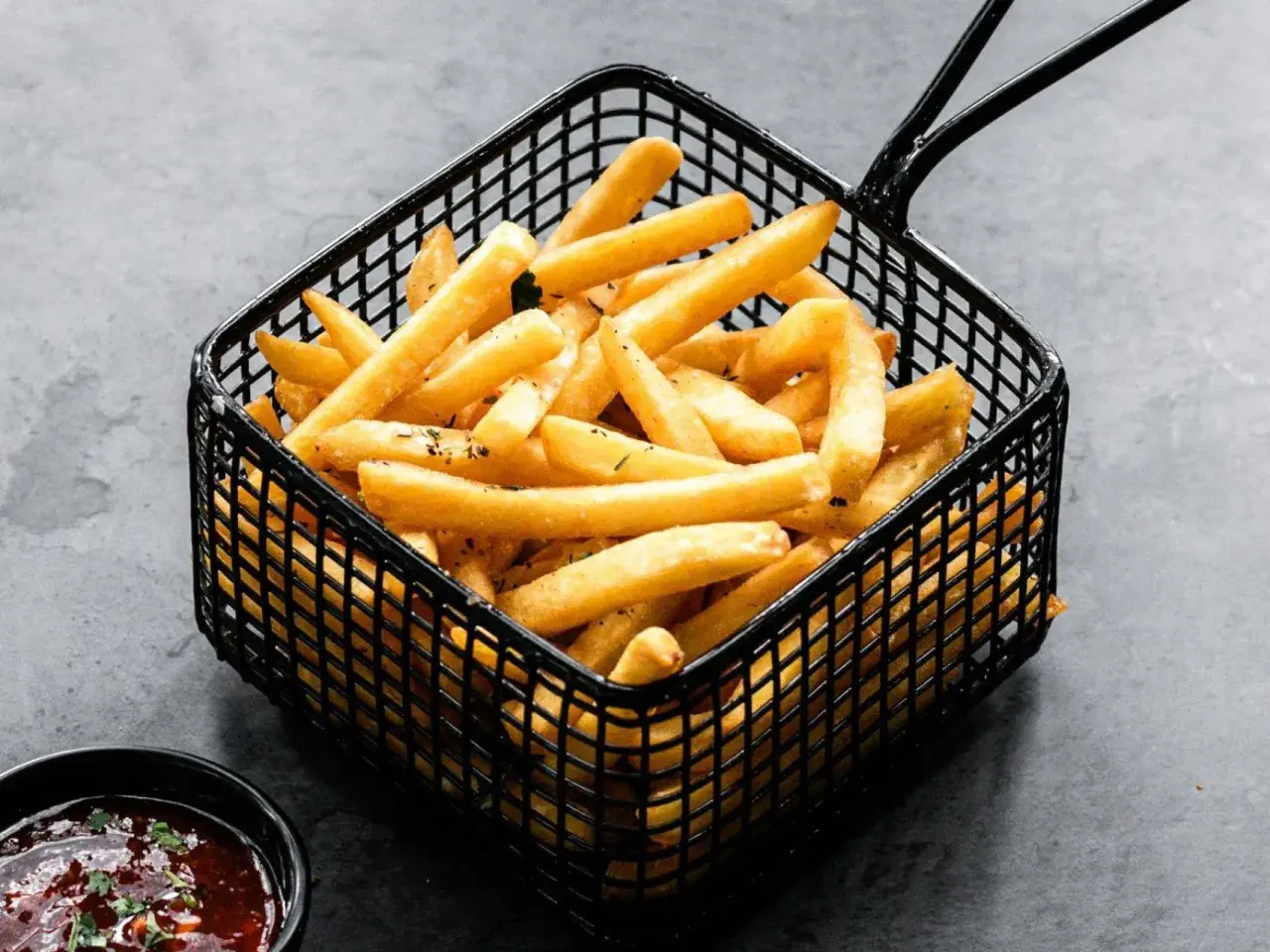 Cesta negra llena de crujientes patatas fritas doradas, listas para ser disfrutadas con una salsa roja.