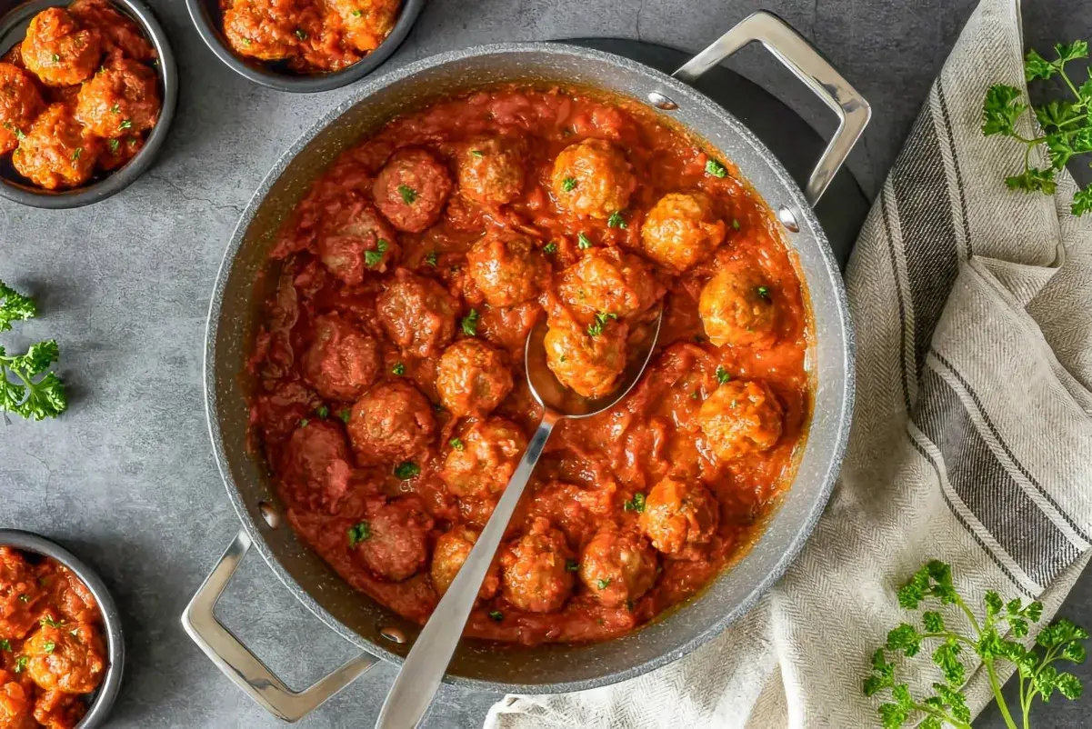Sabrosas almondigas en salsa roja, recién servidas en una sartén, con perejil fresco espolvoreado. ¡Un plato casero irresistible!