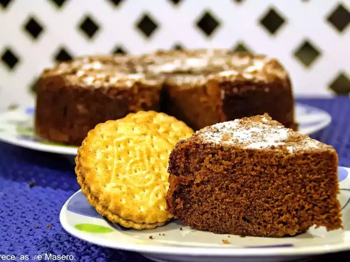 Un trozo de bizcocho de chocolate espolvoreado con azúcar glas junto a una galleta tipo Príncipe.