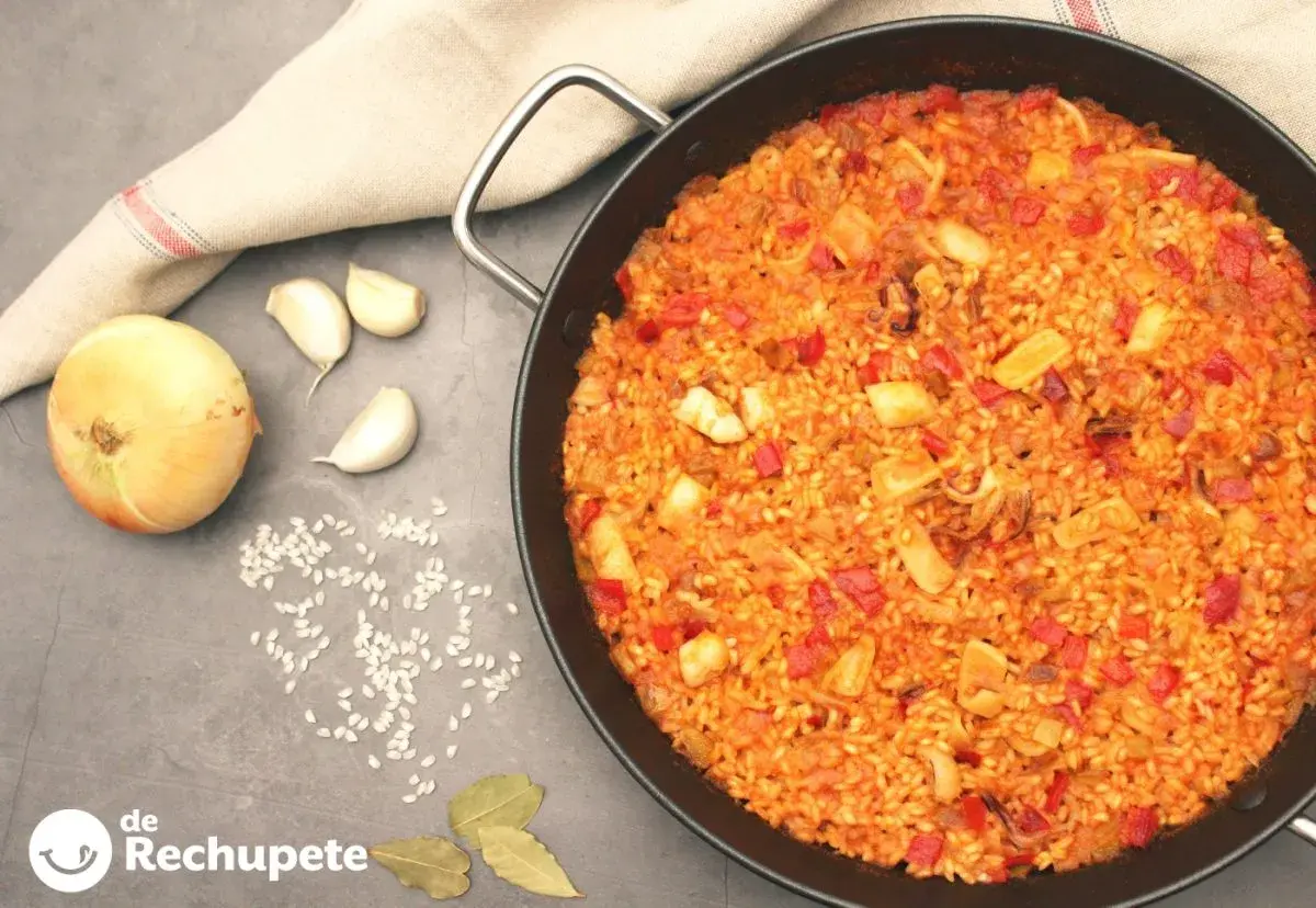 Paella de arroz con calamares, pimientos rojos y especias. Ingredientes frescos como cebolla y ajos acompañan este delicioso plato.