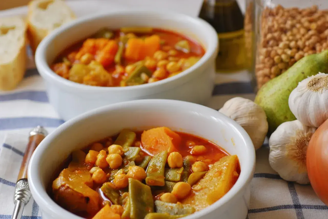 Dos cuencos de olla gitana murciana, un guiso tradicional con garbanzos, calabaza y judías verdes. Acompañado de pan y ingredientes frescos.