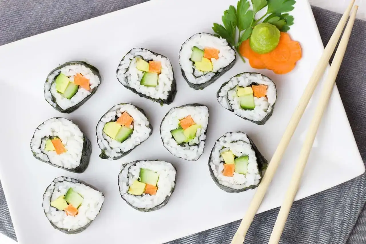 Rollos de sushi vegetarianos con aguacate, pepino y zanahoria, listos para disfrutar con palillos. El arroz para sushi es la base perfecta.