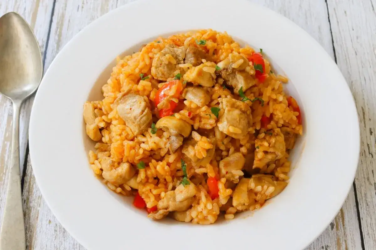 Un plato de arroz con carne, trozos de pollo y pimientos rojos, adornado con perejil.