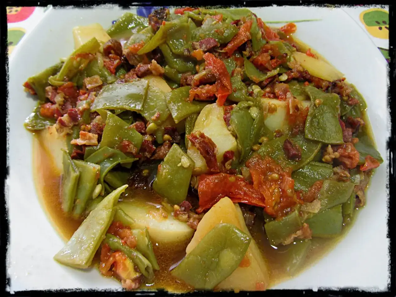 Un plato casero de judías verdes con patatas, trozos de tomate y panceta. Un guiso reconfortante y lleno de sabor.