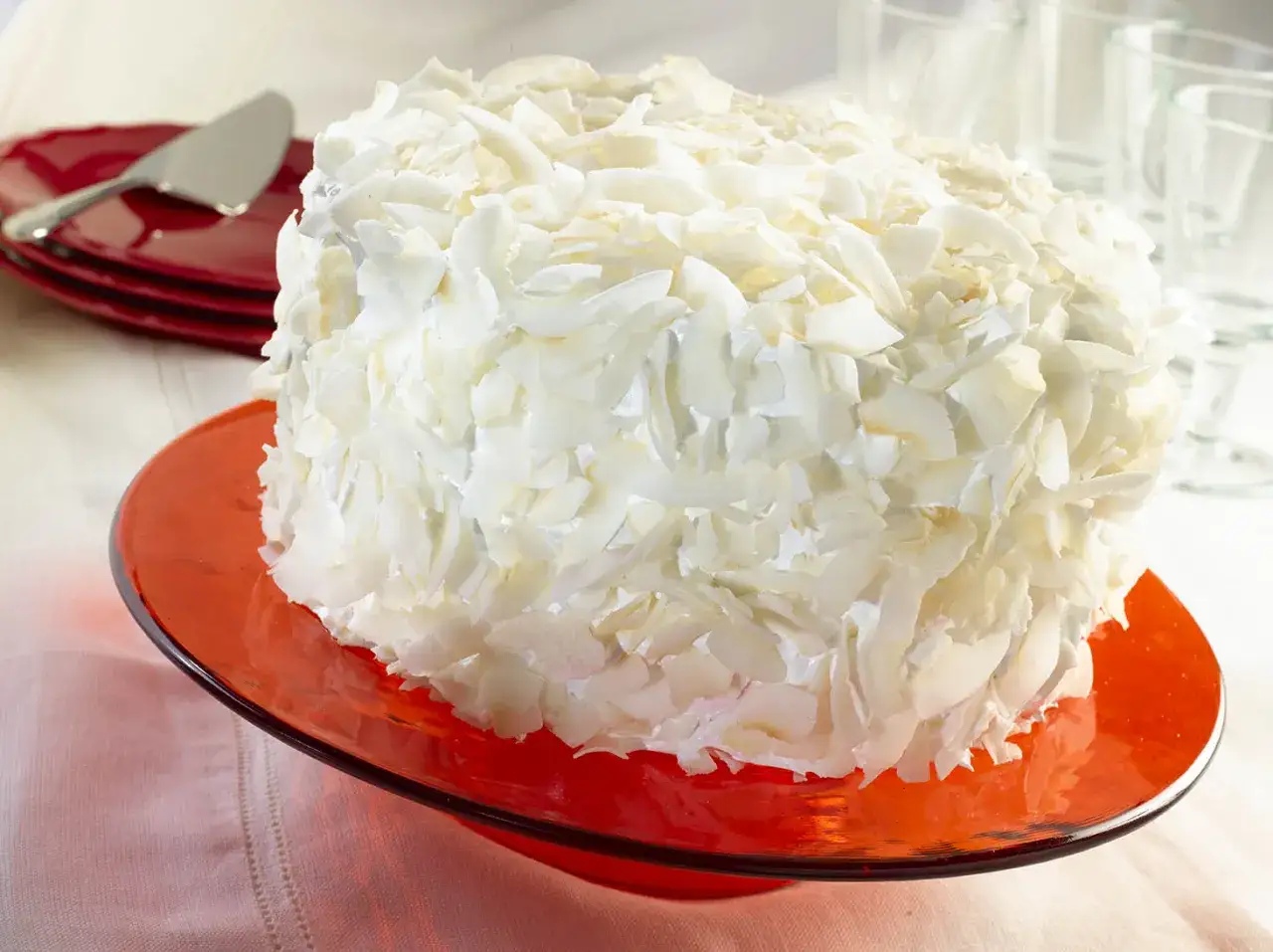 Tarta de coco cubierta de virutas blancas, servida en un plato rojo.