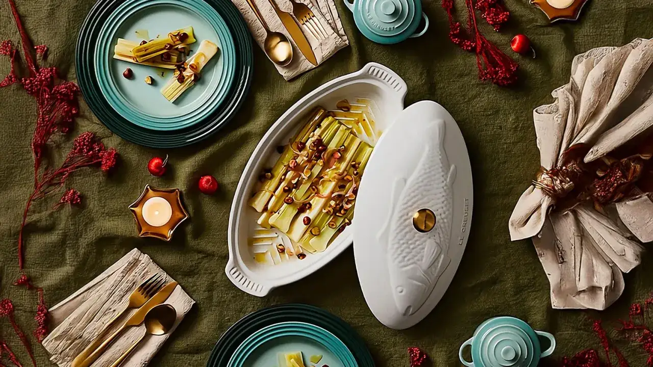Puerros al horno, tiernos y dorados, servidos en una elegante fuente con tapa en forma de pez. Decoraci&oacute;n festiva con velas y frutos rojos.