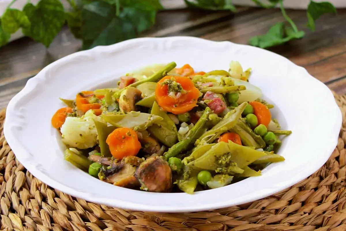Un plato de menestra de verduras con patatas, zanahorias, judías verdes, guisantes y champiñones, todo ello aderezado con una salsa verde.