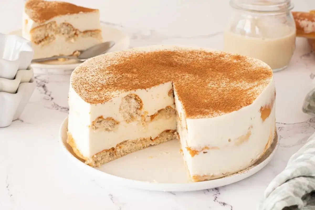 Tarta de horchata y fartons, con bizcocho y crema suave, espolvoreada con canela. Una porci&oacute;n ya cortada espera en un plato.