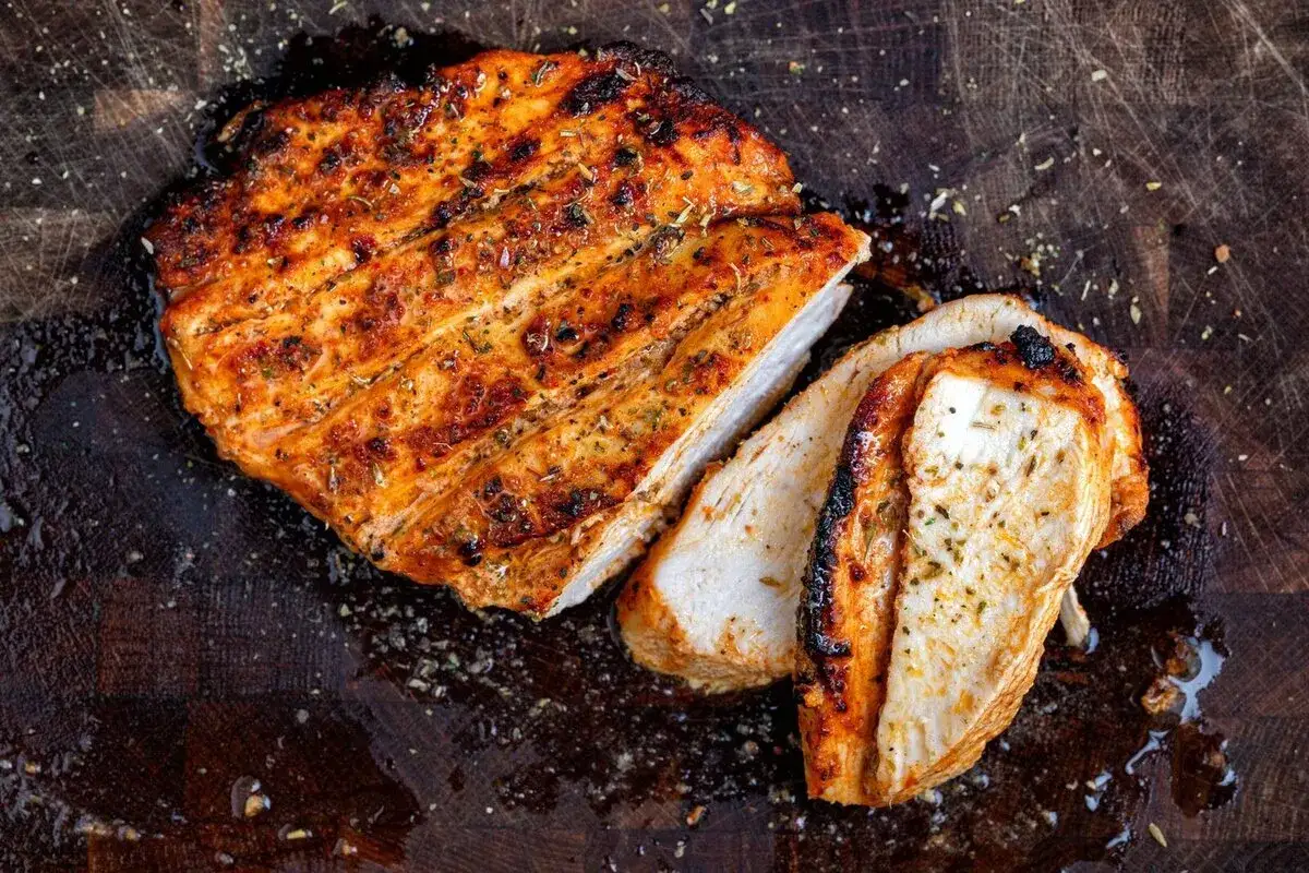 Pechuga de pollo en freidora de aire, jugosa y dorada, cortada en rodajas sobre tabla de madera.