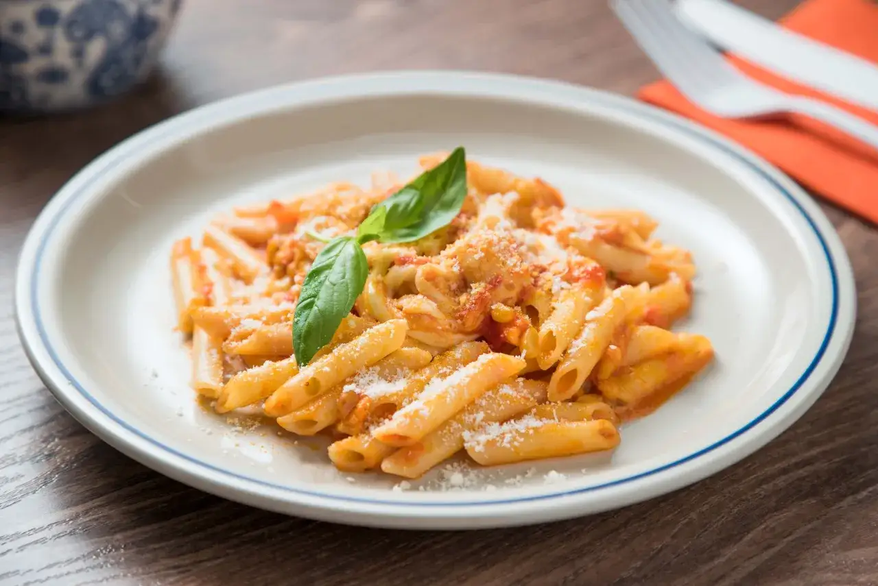 Macarrones con tomate, cubiertos de queso rallado y decorados con una hoja de albahaca fresca. Un plato sencillo y delicioso.