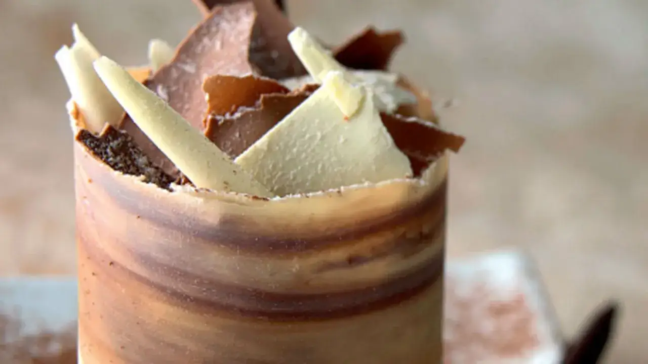 Delicioso mousse de café envuelto en chocolate marmoleado, coronado con virutas de chocolate blanco y oscuro.