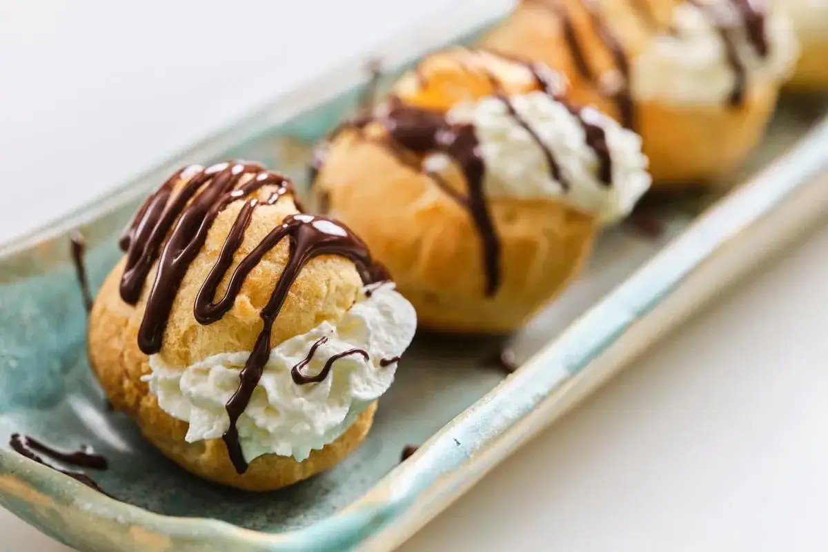 Profiteroles de nata cubiertos con chocolate derretido, servidos en una bandeja.