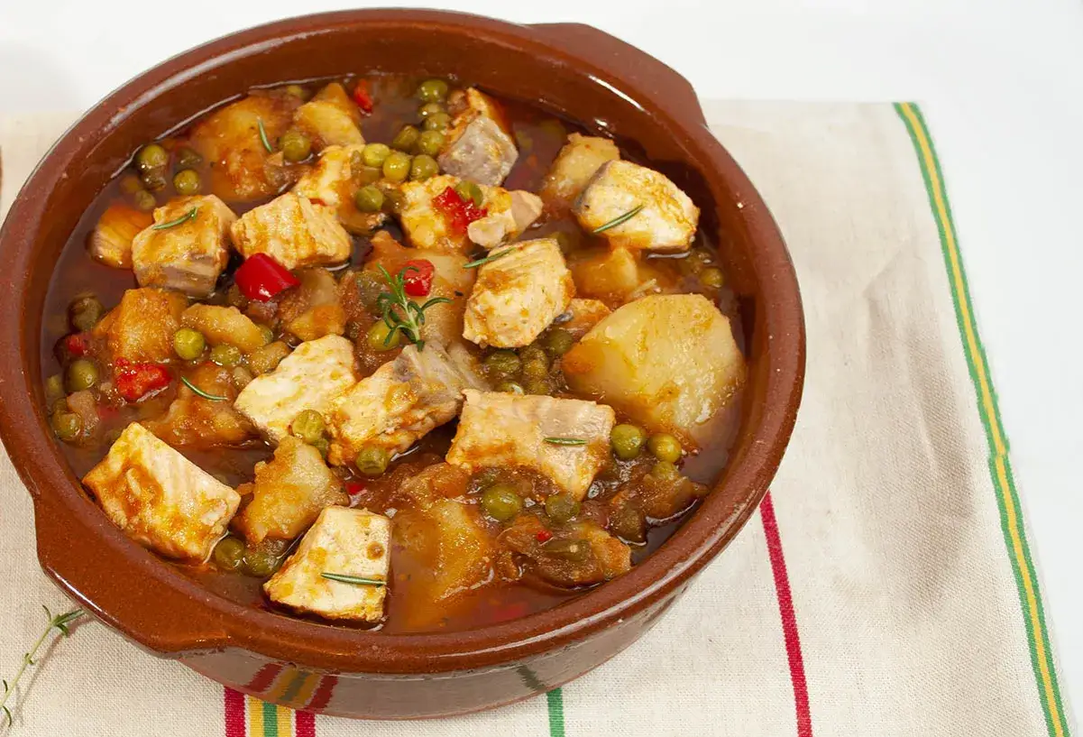Un delicioso marmitako de salm&oacute;n, con trozos de pescado, patatas, guisantes y pimientos rojos en una cazuela de barro.