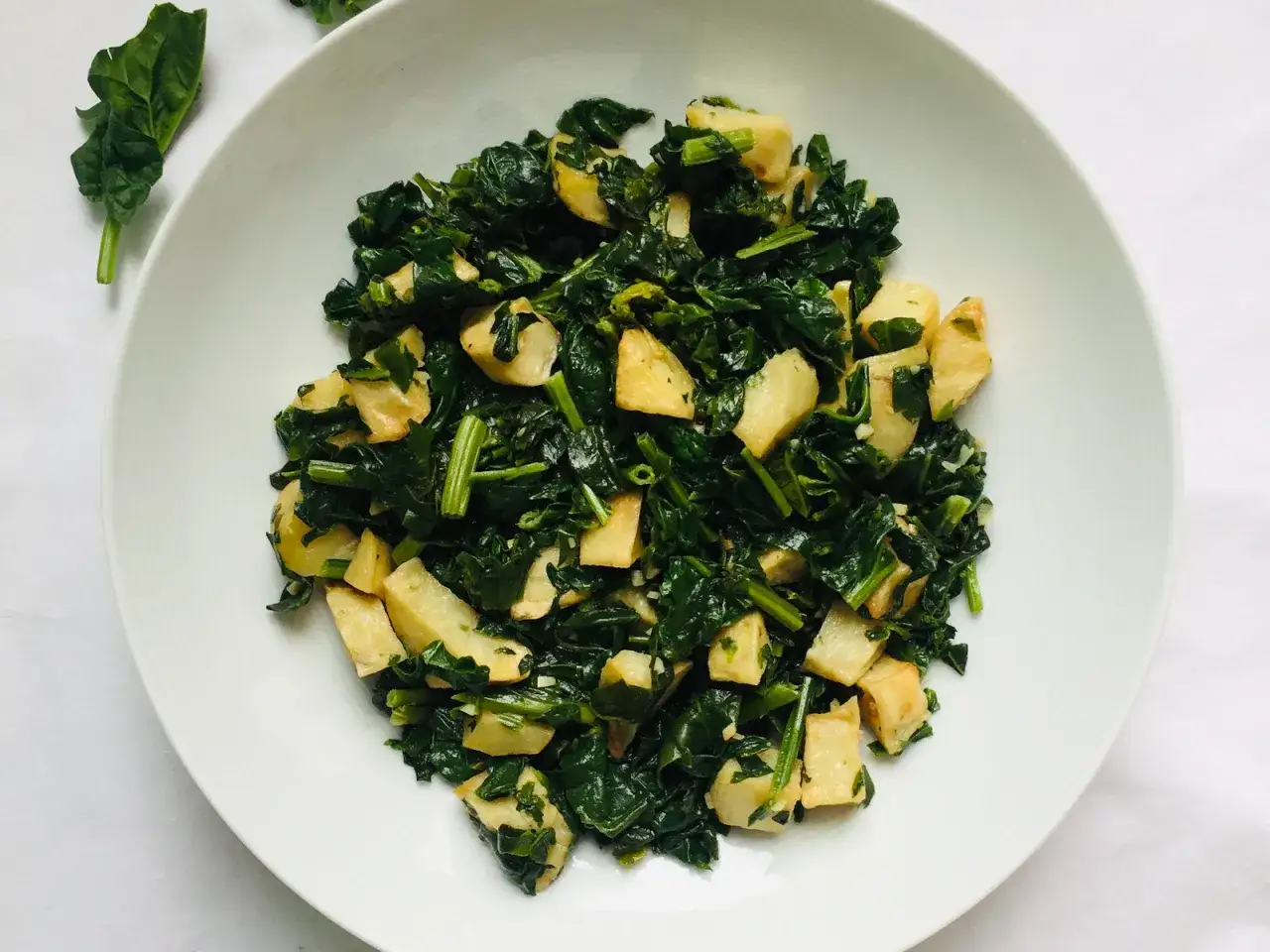 Un plato blanco lleno de espinacas con patatas salteadas, un plato sencillo y nutritivo.
