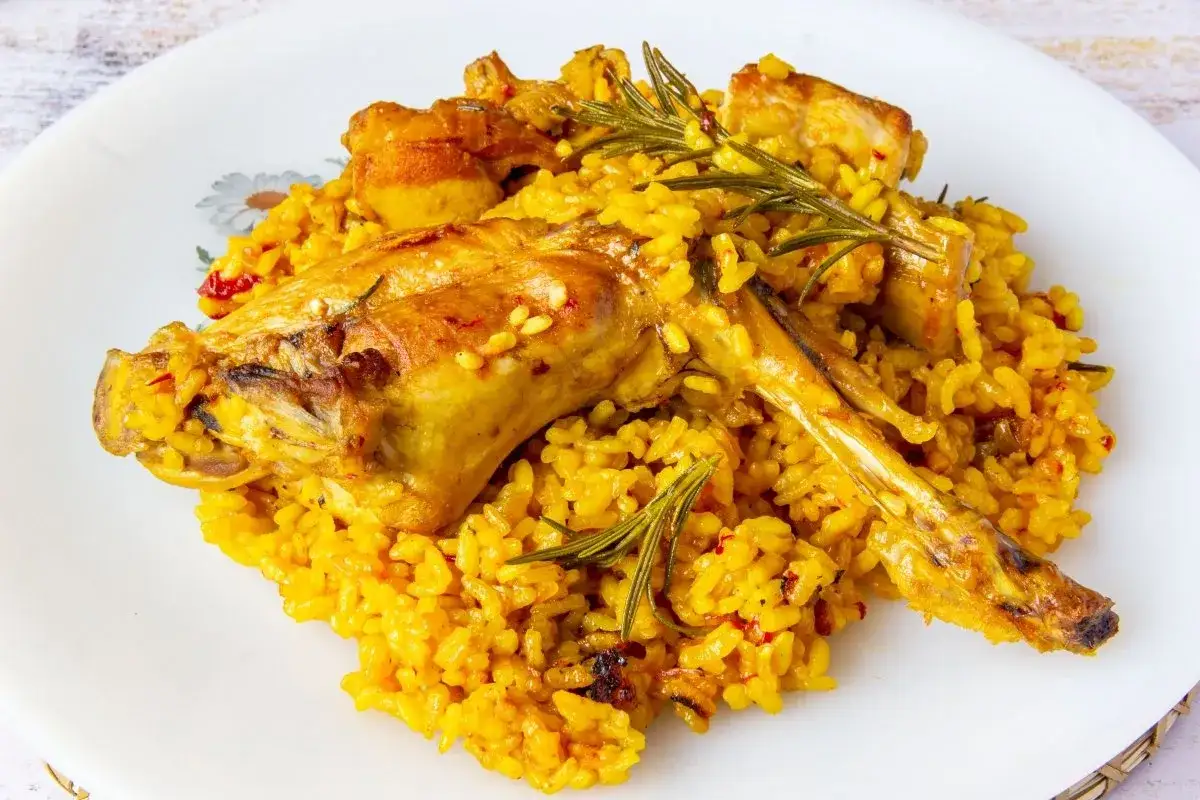 Un plato de arroz con conejo, dorado y sabroso, adornado con romero fresco.
