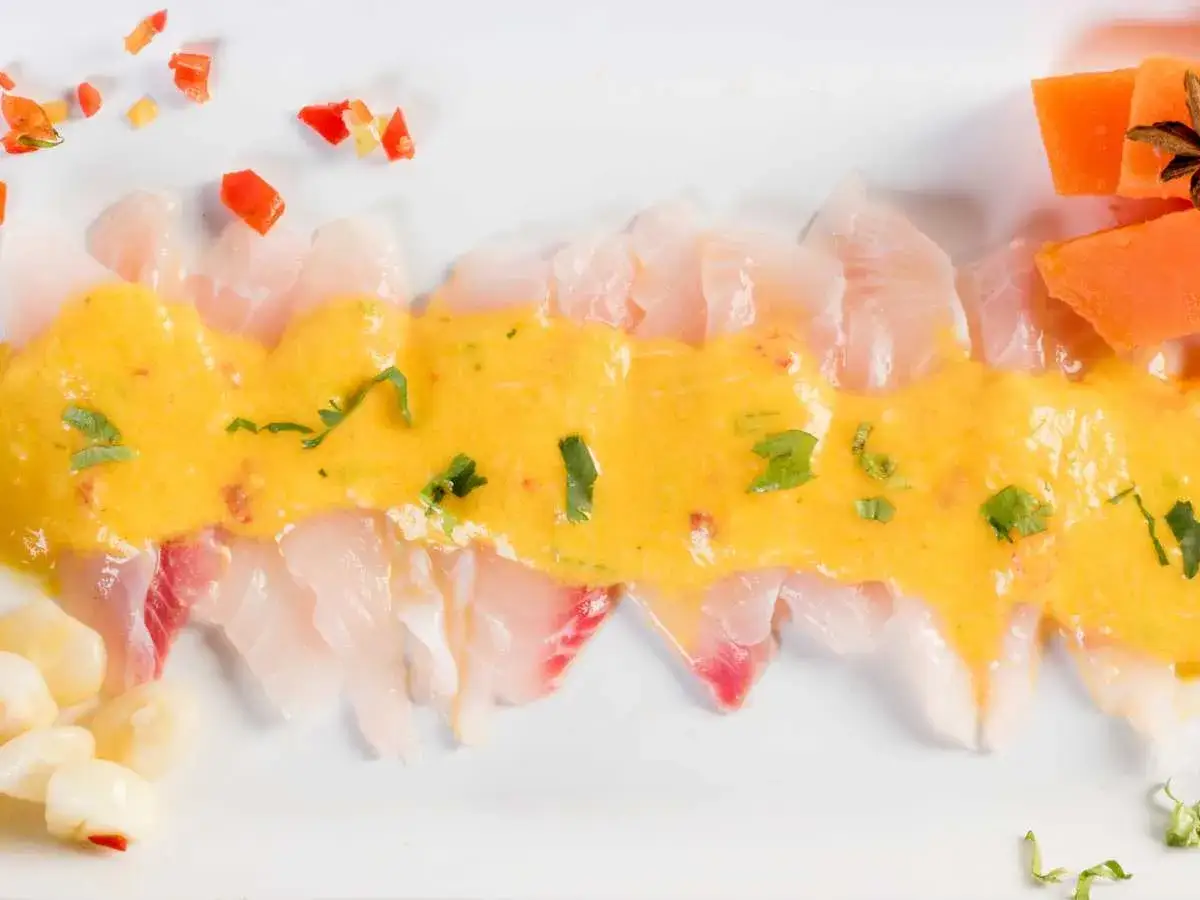 Delicioso tiradito de corvina con salsa de aj&iacute; amarillo, adornado con choclo, pimientos y camote.
